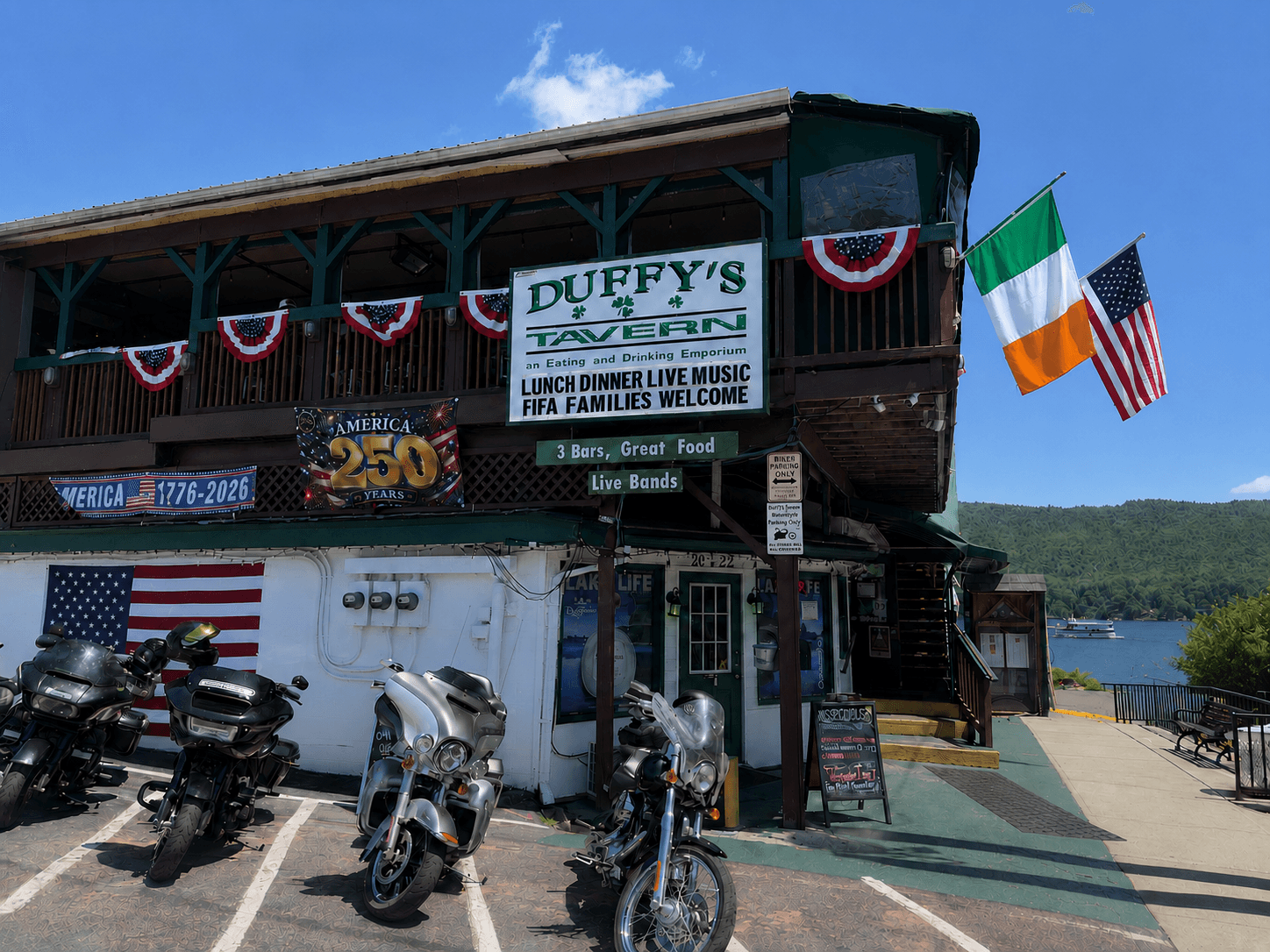 Duffy's Tavern storefront on a sunny day, motorcycles parked out front, Irish and American flags flying beside the entrance