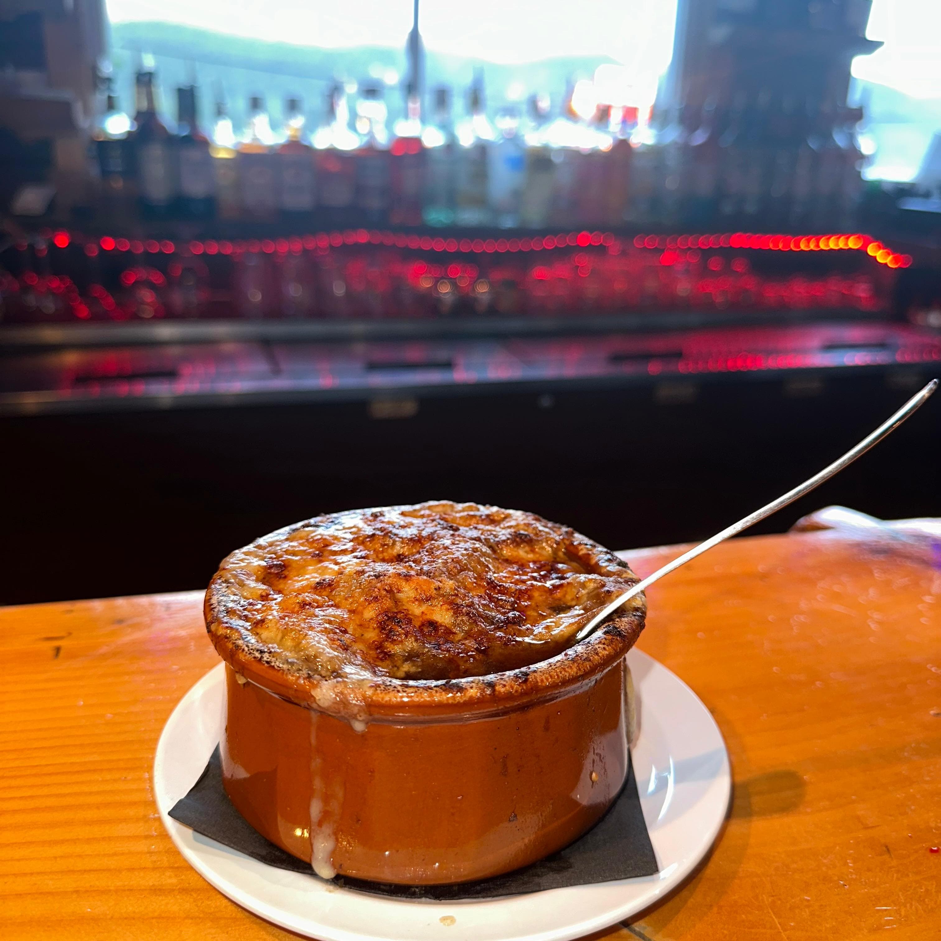 Crock of French onion soup topped with bubbling melted cheese, served at the bar