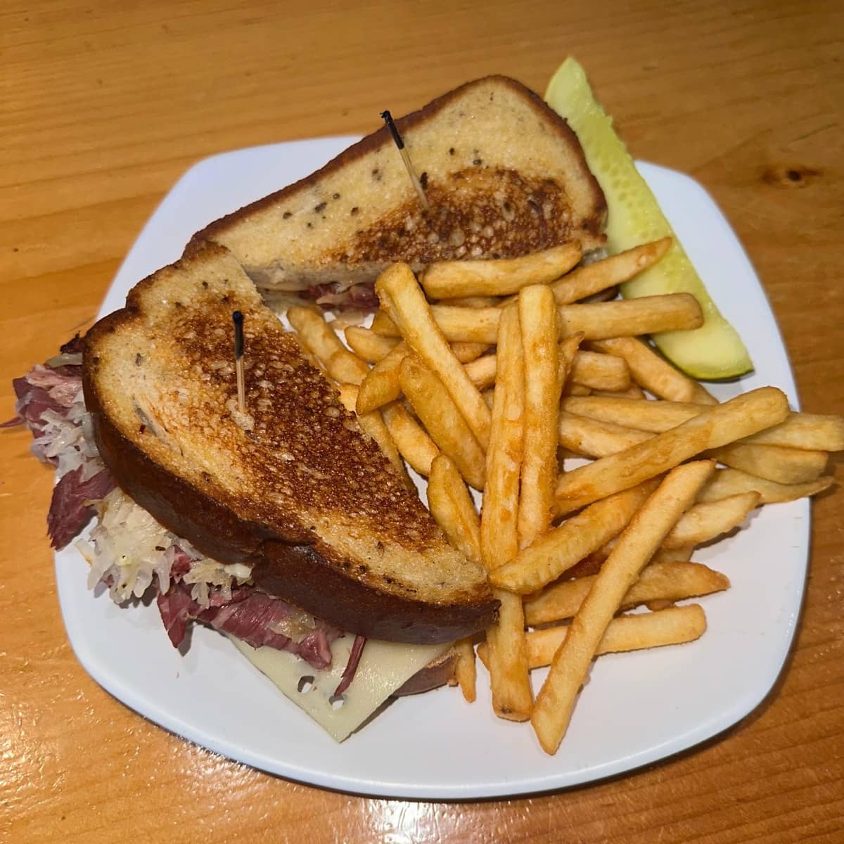Grilled Reuben sandwich stacked with corned beef and Swiss, served with fries and a pickle
